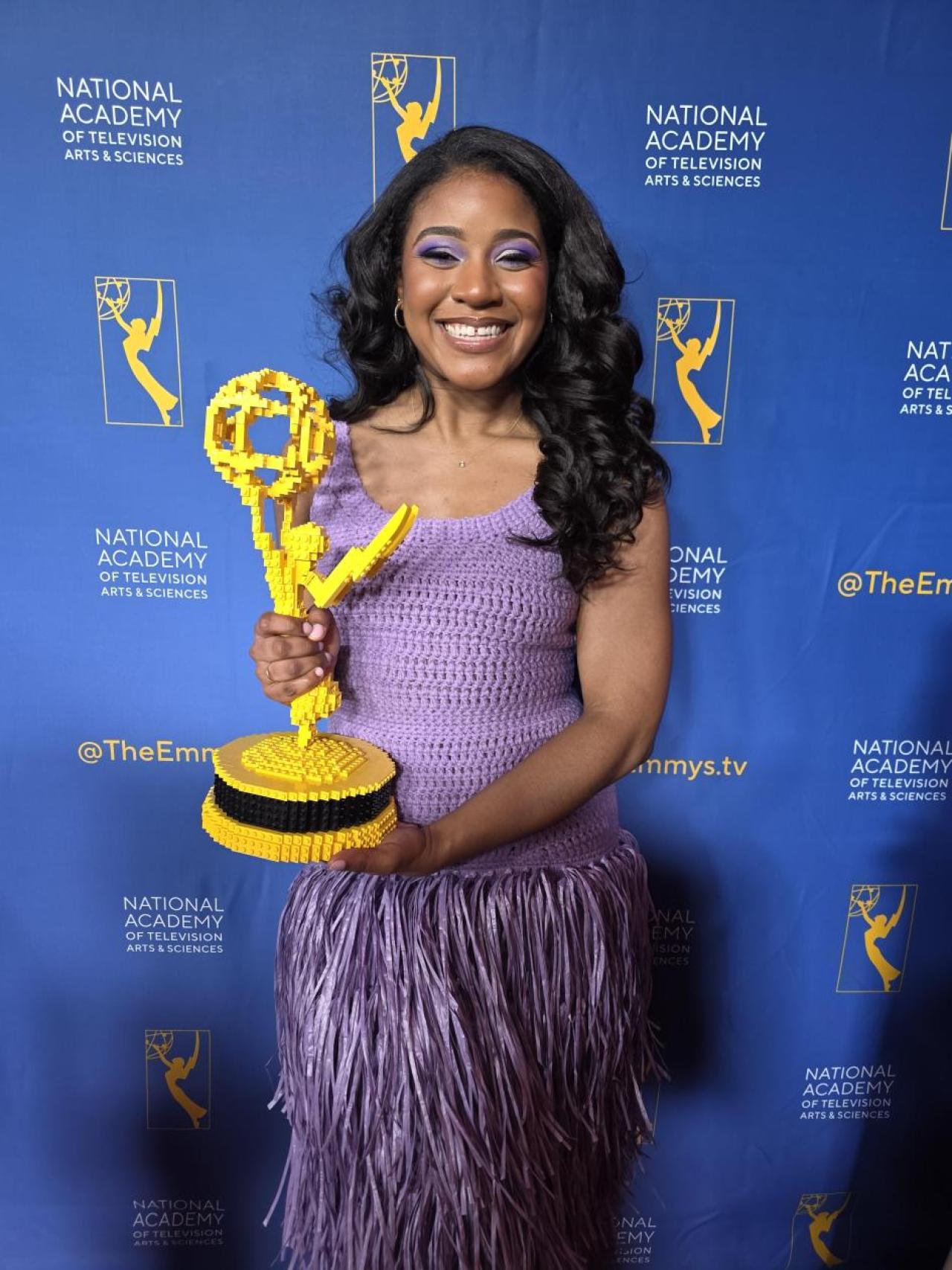 Woman in purple dress holding an Emmy Award
