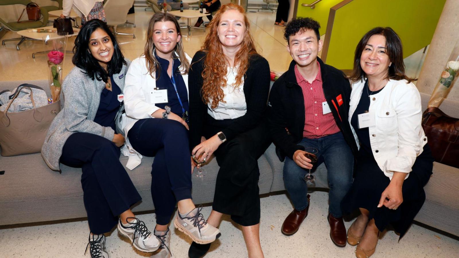 five individuals seated on couch posing for photo.