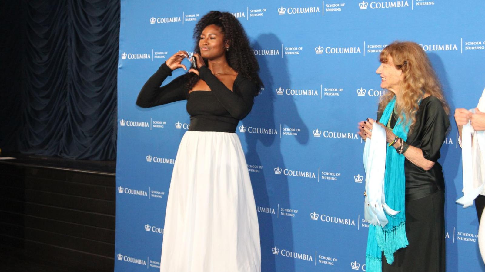 Nursing graduate making heart symbol before receiving pin on stage.