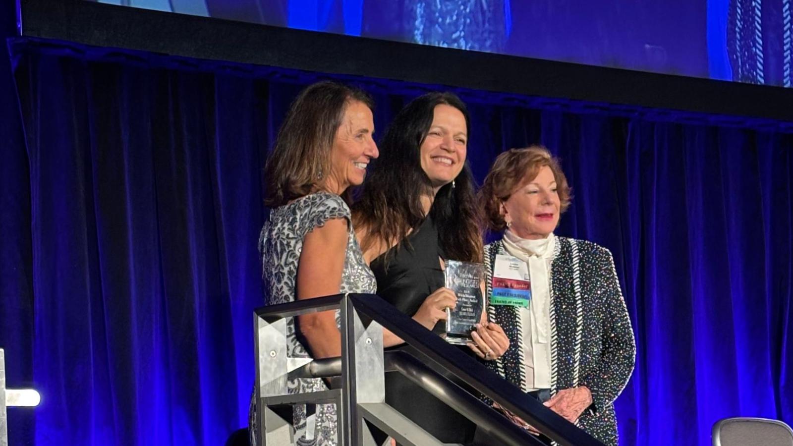 Award winner posting with two presenters on stage