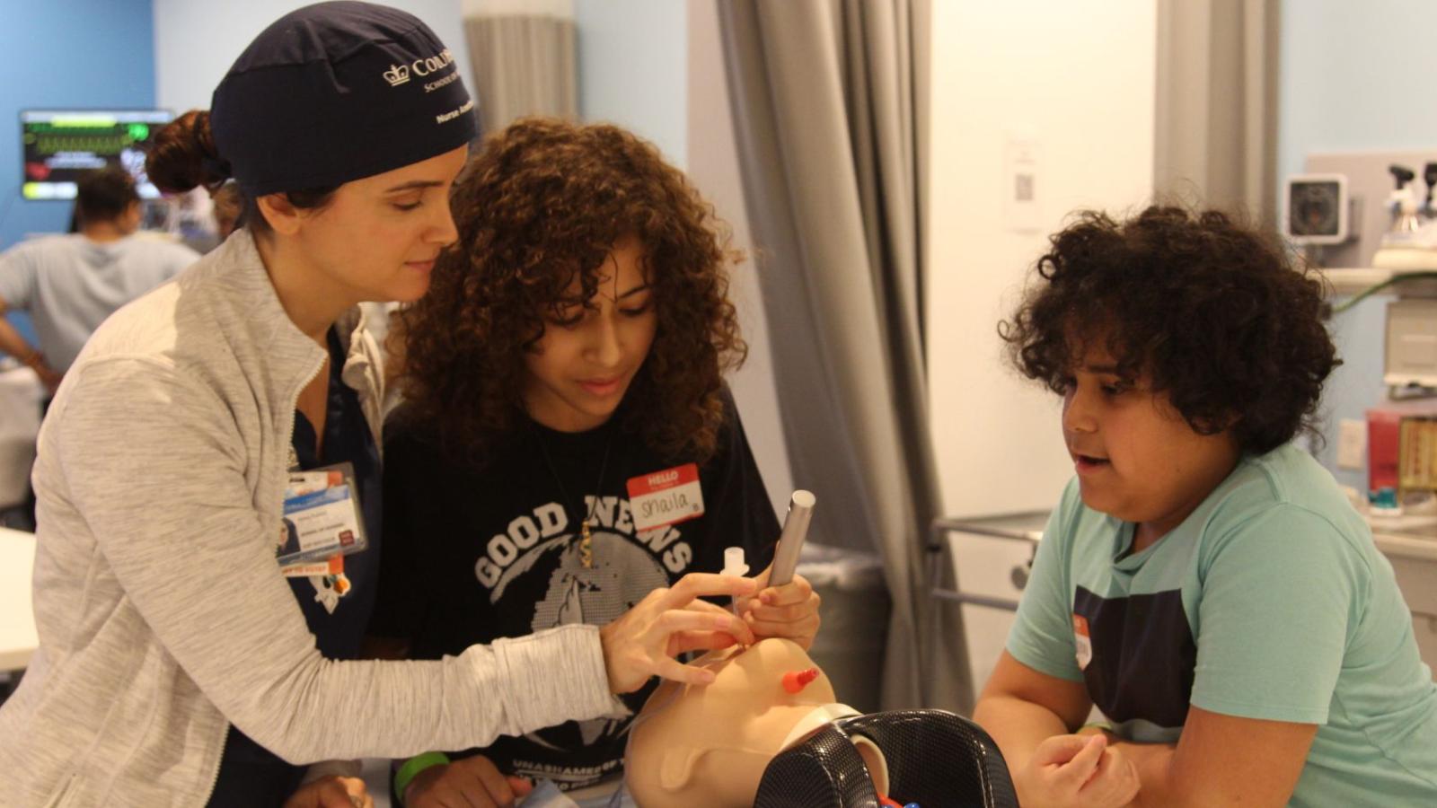Nursing student helping two middle schoolers in a simulation lab