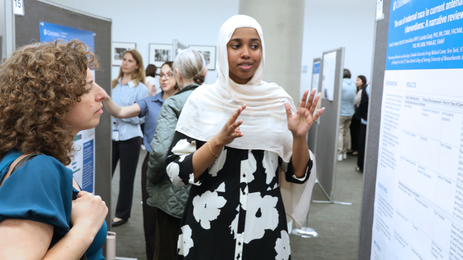 A PhD student presents her research poster to a woman with curly hair