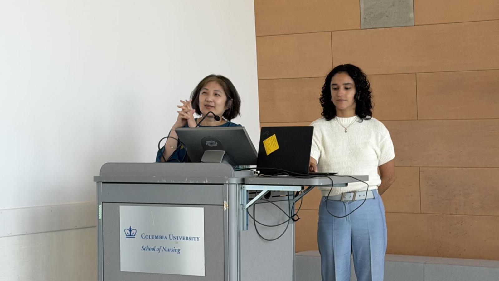 Yuhui and Isabel speak at podium about the order of events at 2026 Global Celebration