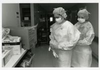 black & white photo of two nursing students helping each other get their personal protective equipment on