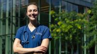 Female nursing student standing proudly outside Columbia Nursing building.