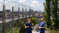 Two students talking in roof garden with city skyline in the background.