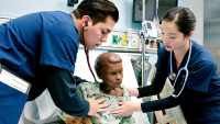 Two students practicing clinical pediatric care on a manikin in a simulation room.