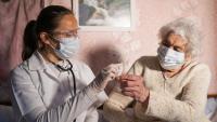Home health staff wearing mask giving medicine to a senior woman at her home.