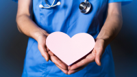 Nurse in blue scrubs holding a pink heart