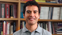 Headshot of Columbia Nursing PhD graduate, David Lopez Verenos, against a wall of books