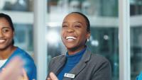 Three nursing executives smile and laugh during a meeting in a glass-walled conference room.