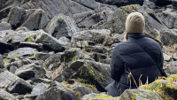 A young woman sitting on rocks looking out at the water