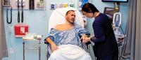 Actor posing as a patient with a nurse caring for him in a hospital simulation setting.