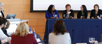 A moderator and four panelists present to an audience at a conference.