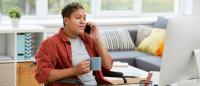 Person in wheelchair on telephone working at computer drinking coffee