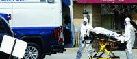 Medical workers load a deceased body into an ambulance while wearing masks and personal protective equipment (PPE)