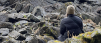A young woman sitting on rocks looking out at the water